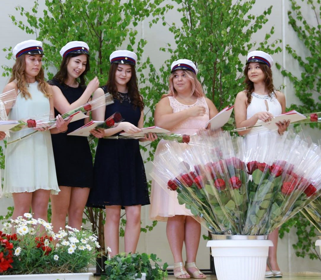 Valkeakosken ammattiopisto, VAAO. Viisi valmistunutta opiskelijaa seisoo rivissä. Heillä on käsissään punaiset ruusut. Heillä on päässään valkoiset ylioppilaslakit.