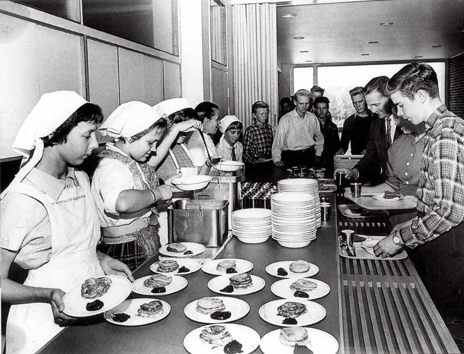 Valkeakosken ammattiopisto, VAAO, vanha mustavalkoinen kuva opiskelijaravintolasta, ehkä 1960-luvulta. Opiskelijat tarjoilevat päivän lounasta, keitto ja ohukaiset, linjastossa.