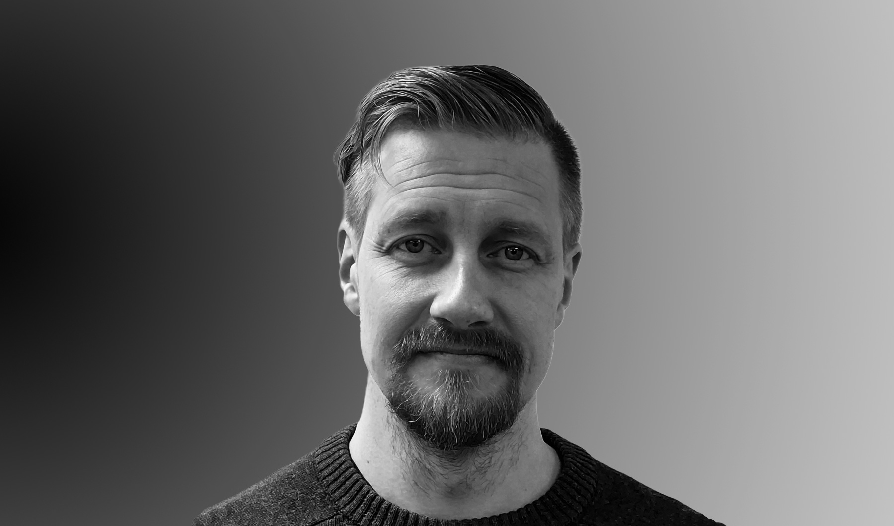 Mustavalkoisessa kuvassa parrakas henkilö katsoo suoraan kameraan