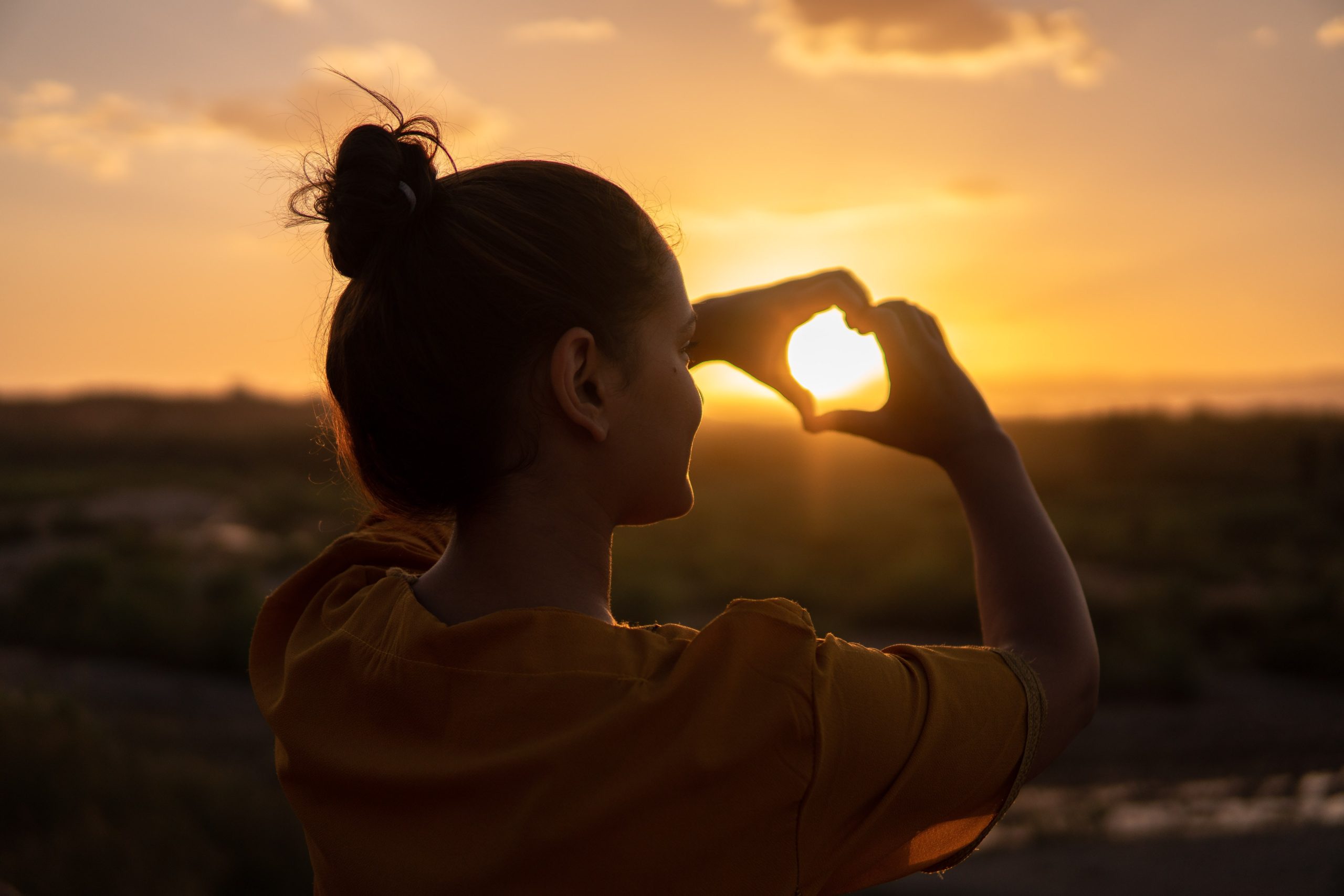 Valkeakosken ammattiopisto, VAAO, henkilö tekee käsillä sydämen kohti auringonlaskua.