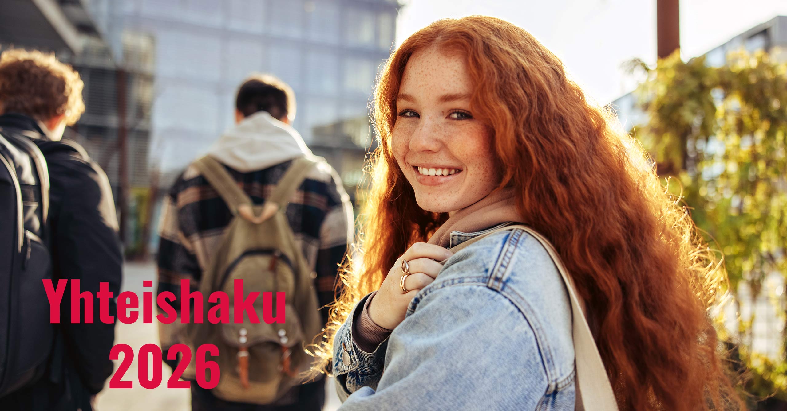 Punahiuksinen tyttö, reppu selässä, katsoo kameraan. edellä kävelee kaksi poikaa reput selässä. Toisella pojalla on punaiset kiharat hiukset ja toisella tummat, molemmilla lyhyet hiukset. He kaikki ovat matkalla Valkeakosken ammattiopistoon.