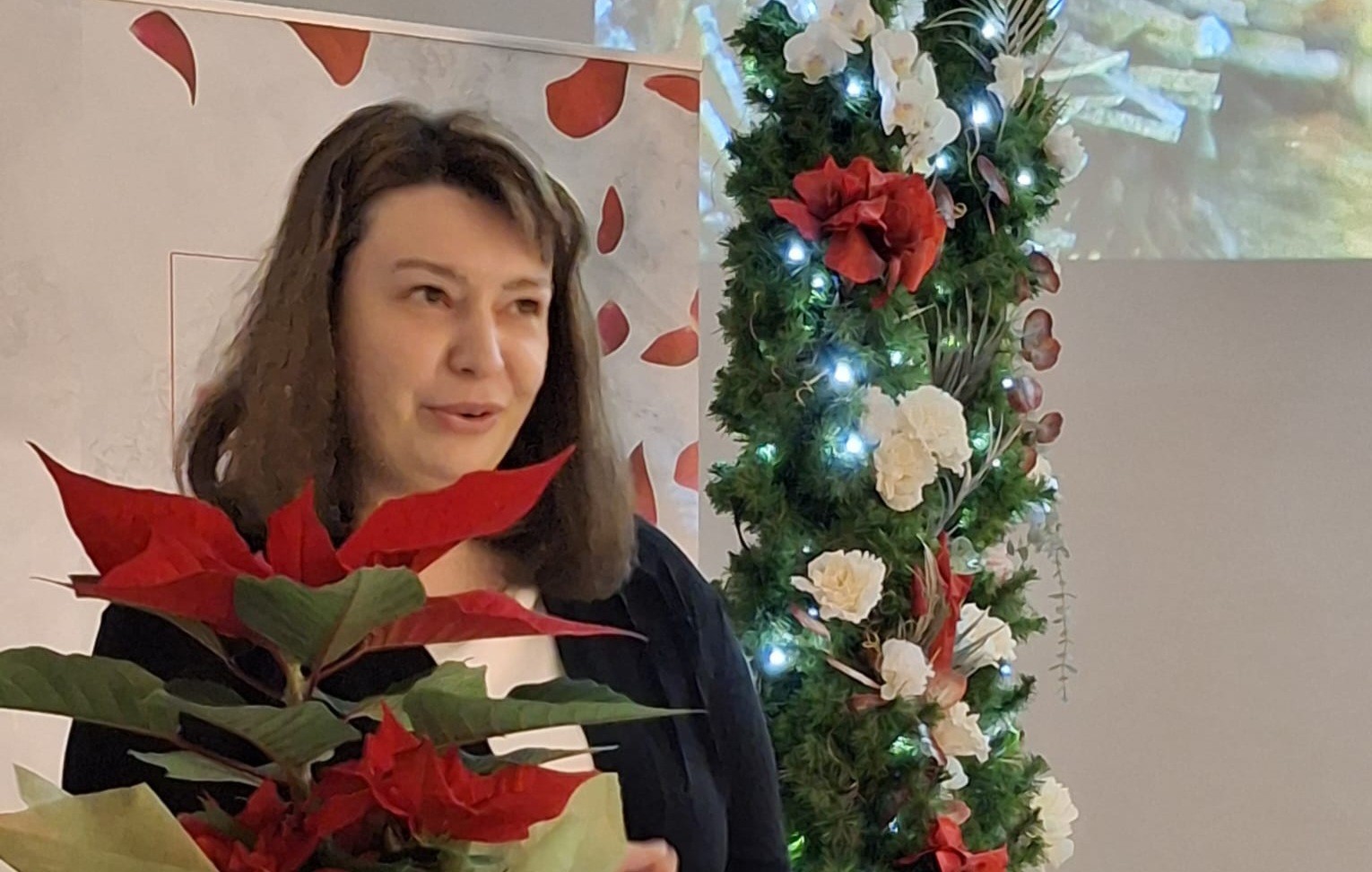 Valkeakosken ammattiopisto, VAAO, Pitkähiuksinen henkilö pitää juhlapuhetta, kukka edessä pöydällä.