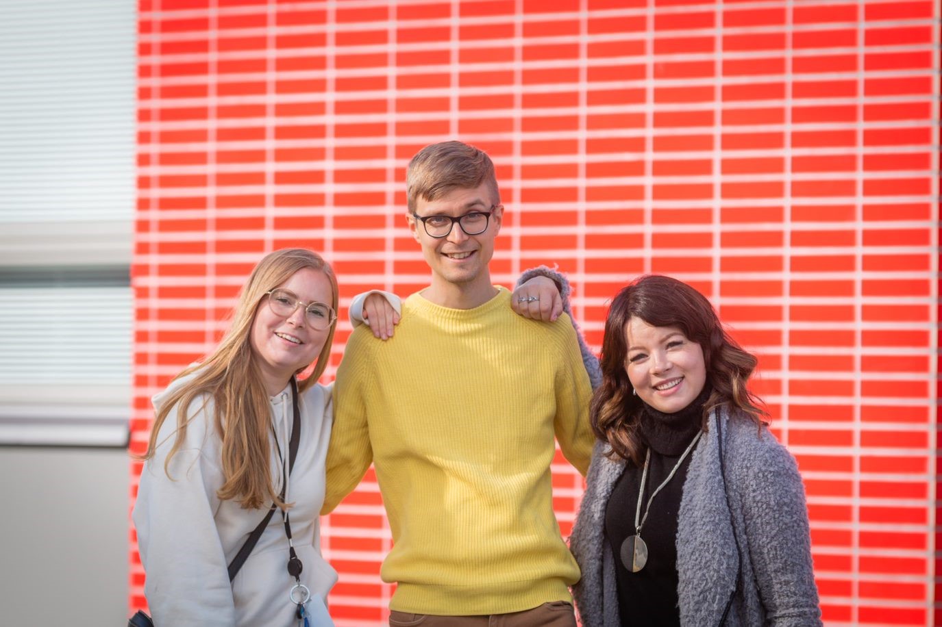 Valkeakosken ammattiopisto, VAAO. Kolme henkilöä seisoo vierekkäin pihalla hymyillen kameralle.