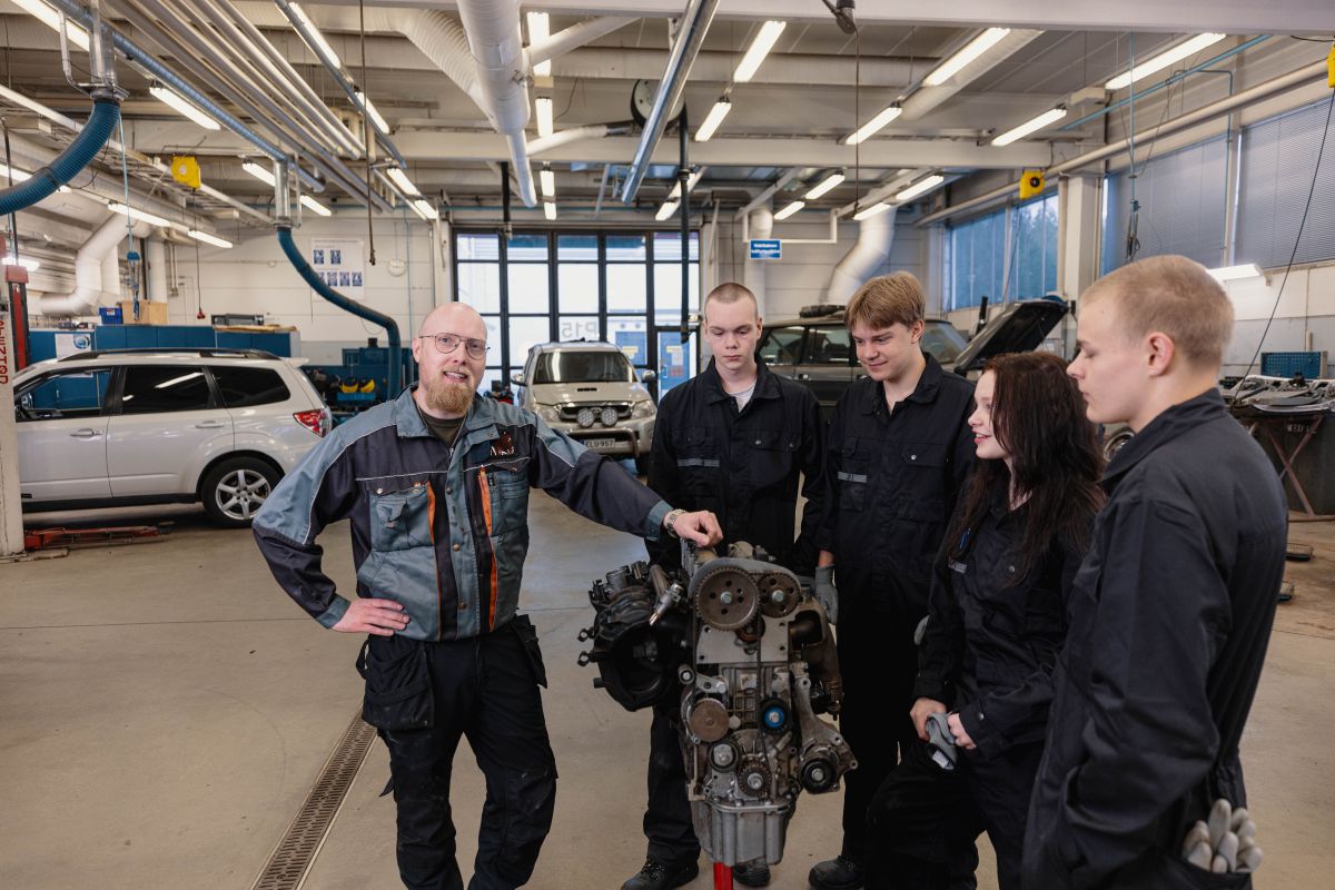 Autoalan opsikelijat moottorin ympärillä opettajansa kanssa.