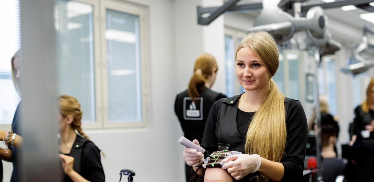 Hiusalan opiskelija tekee mallinukelle permanettia VAAOn kampaamossa.