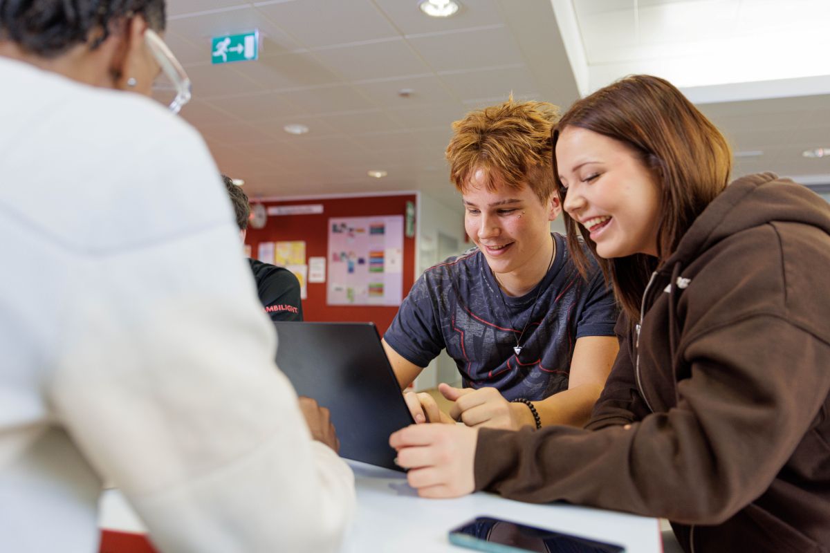 Kaksi hymyilevää opsikelijaa katsoon sisältöä kannettavalta tietokoneelta pöydän ääressä.