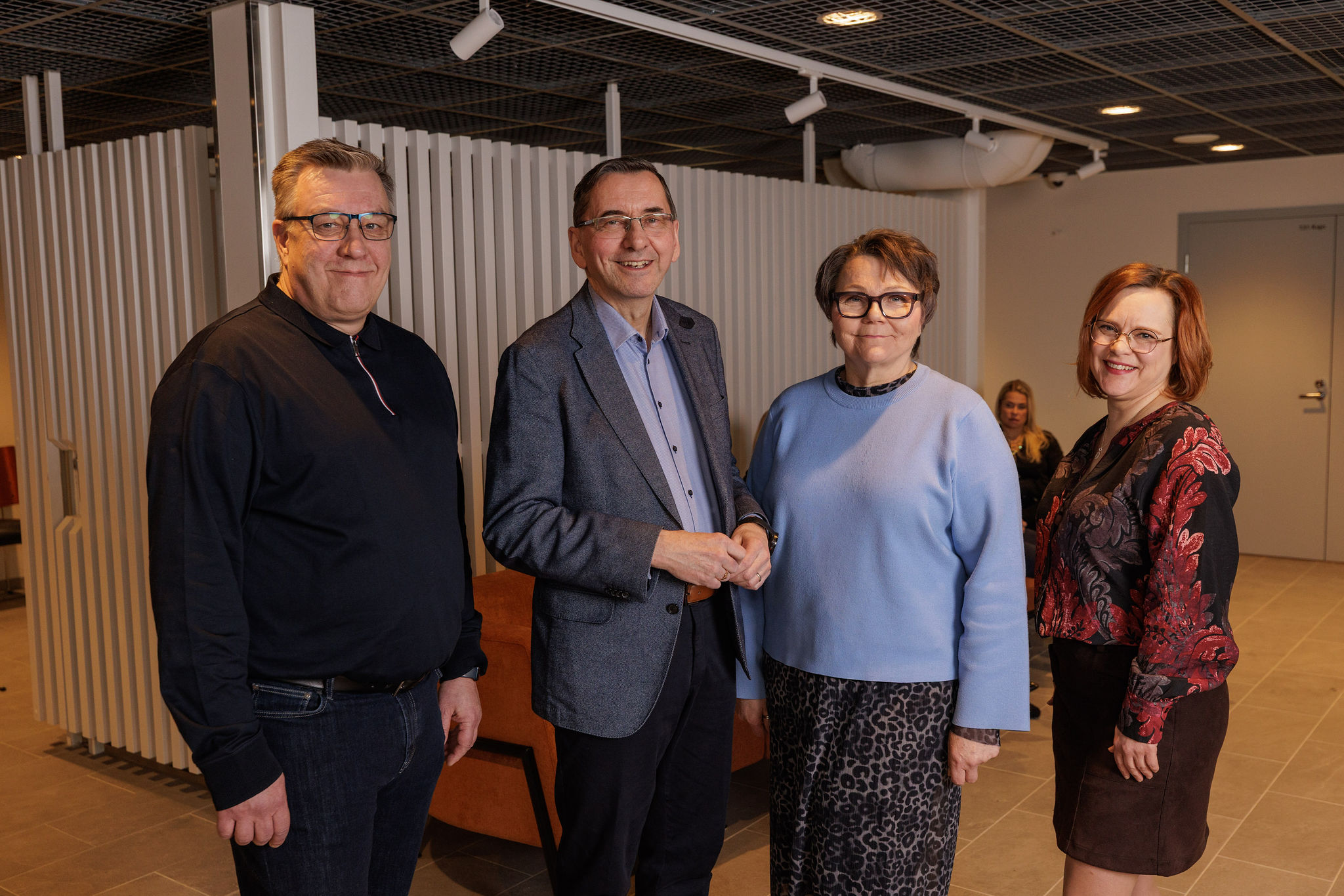 neljä henkilöä seisoo vierekkäin kuvassa ja hymyilee kameralle. Kaikilla silmälasit.