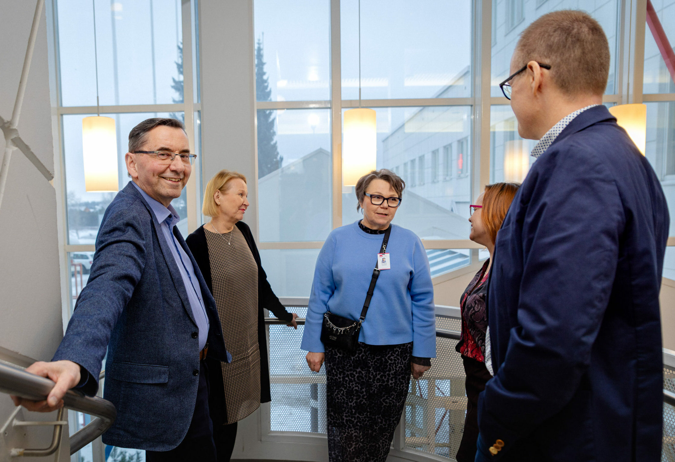 VAAOn johtohenkilöitä koulun pääportaikossa. Rehtori katsoo kameraa.