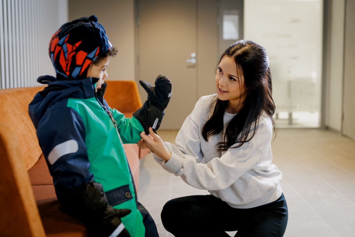 Lähihoitajaopiskelija auttaa lasta pukeutumaan.