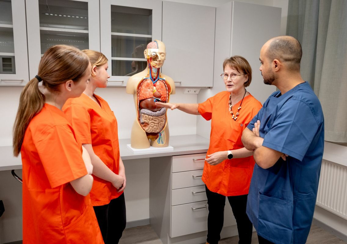 Kolme hoitajaopiskelijaa seuraa, kun opettaja havainnolistaa ihmisen sisäelinten toimintaa torsomallista.