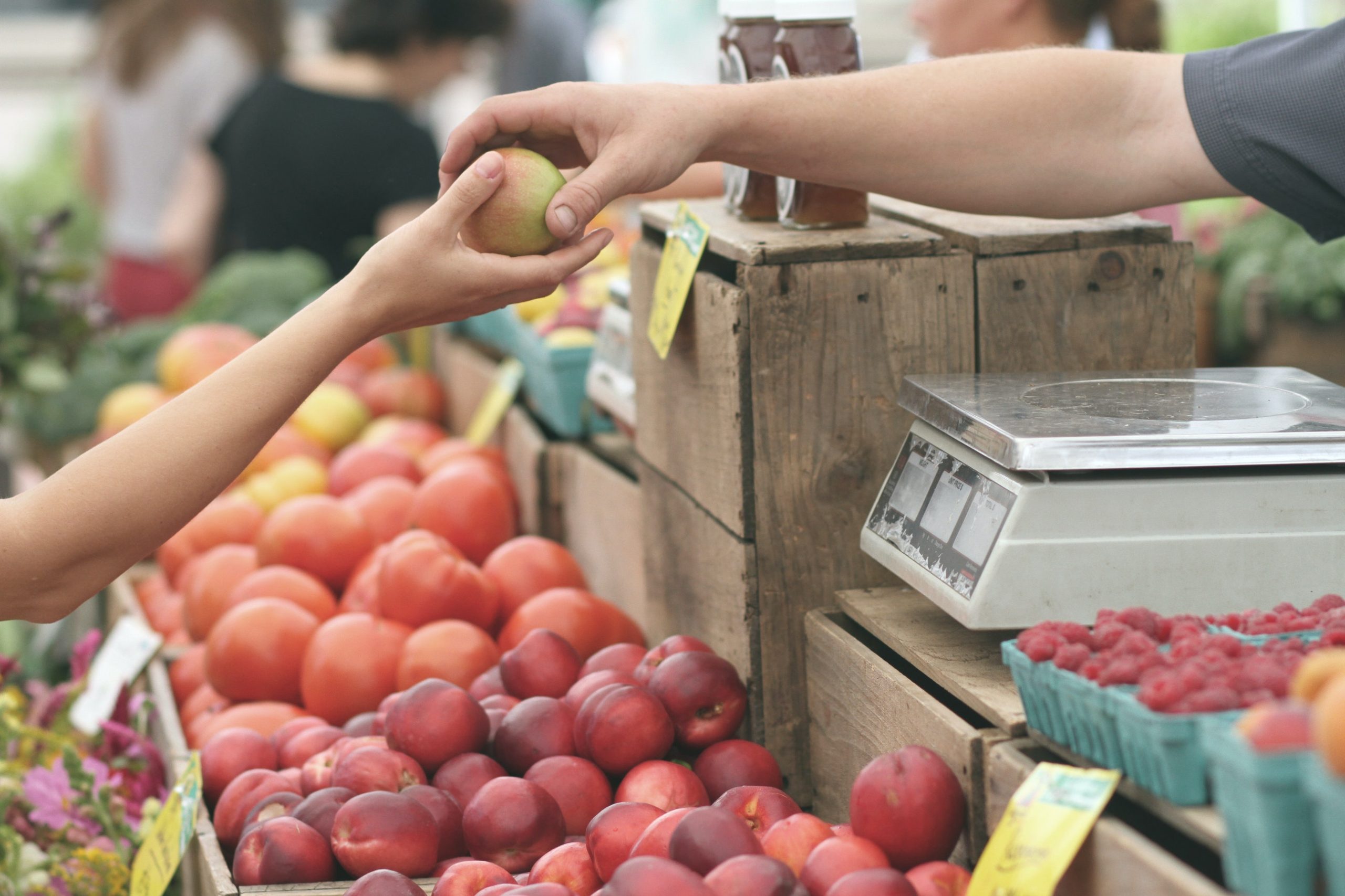 Valkeakosken ammattiopisto, VAAO. Lähikuva ruokatorista. Myyjän käsi ojentaa asiakkaan käteen omenaa.