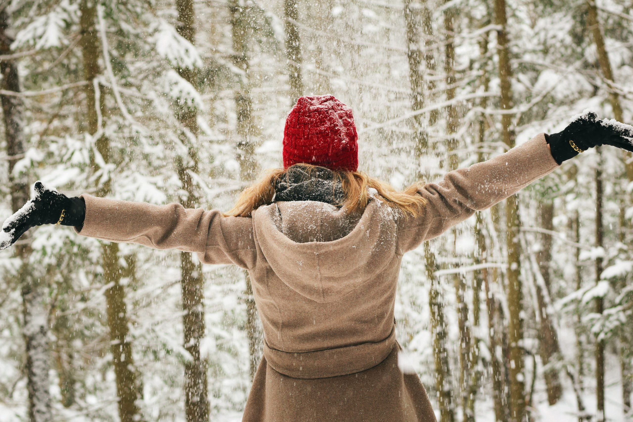 Valkeakosken ammattiopisto, VAAO. Henkilö seisoo selin kameraan talvisessa maisemassa. Hänellä on päällään punainen pipo, beige takki ja mustat hanskat. Hänen päälleen sataa lunta.